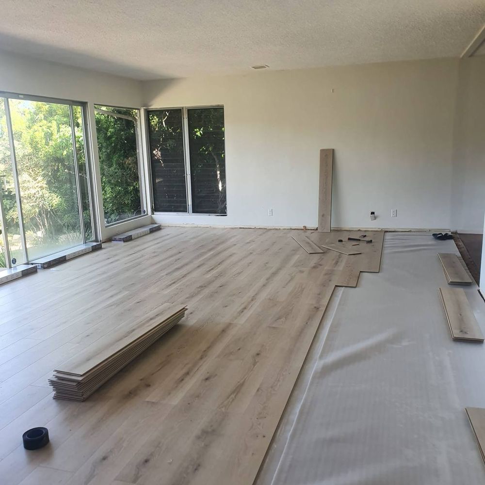 Plank flooring being laid across an open living area over underlay — flooring installation service in Denver