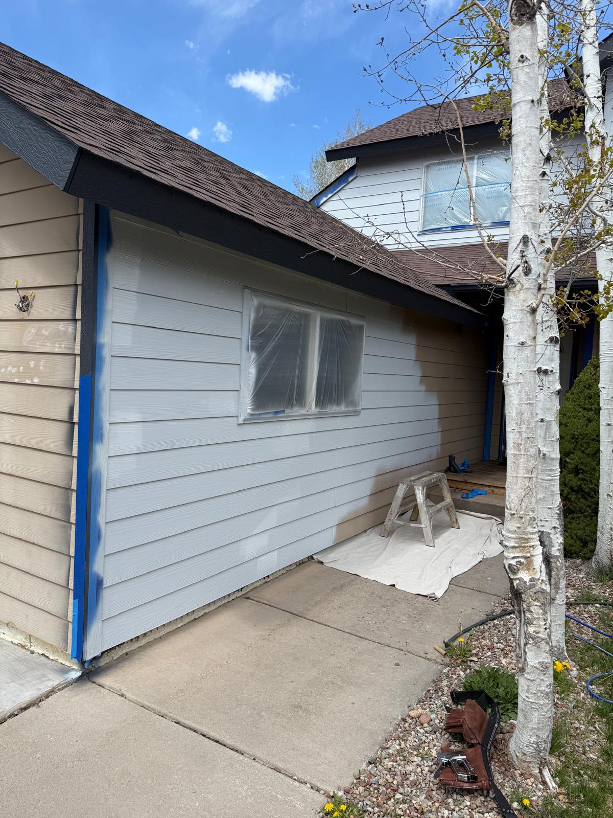 House siding masked with tape and sheeting ready for a colour change — exterior painting service in Denver