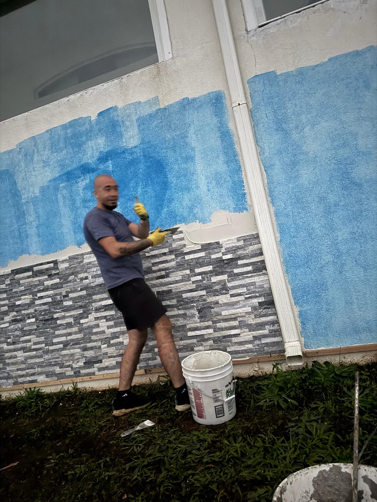 Painter cutting in above new stone veneer on a house exterior — exterior painting service in Denver