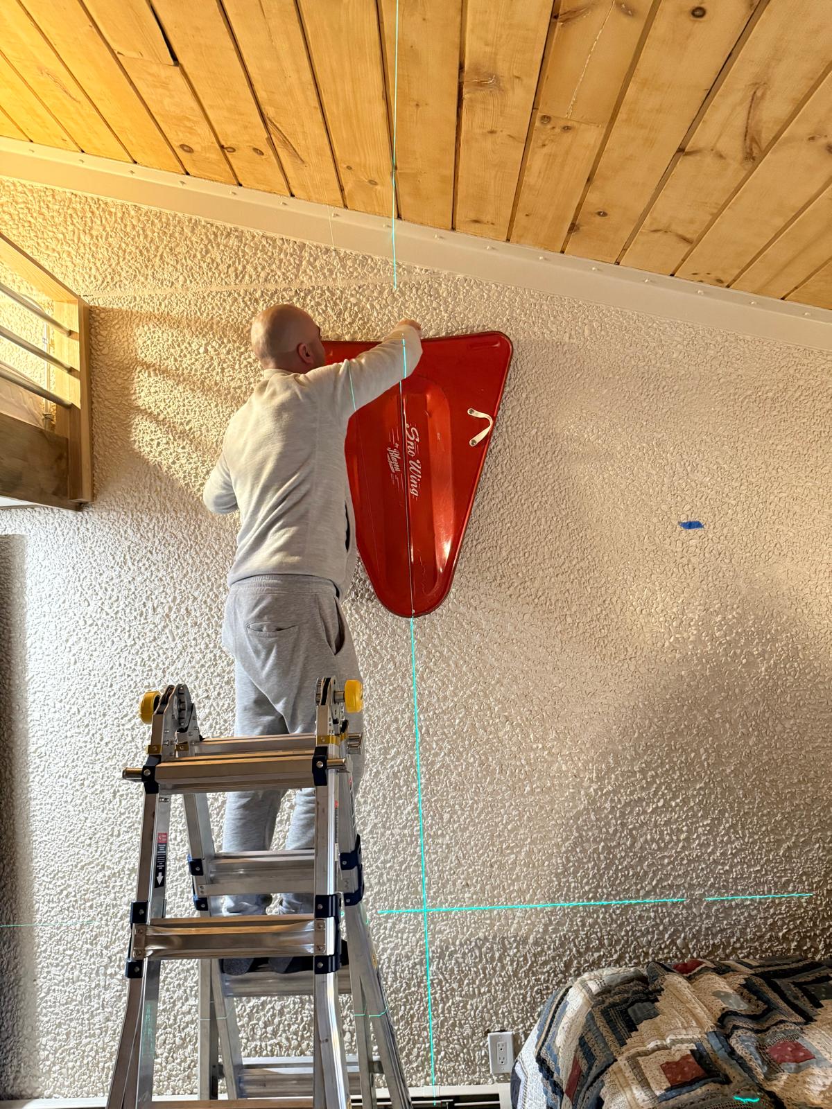 Installer holding a large red sculptural wall piece level against a textured wall — mounting and installation service in Denver