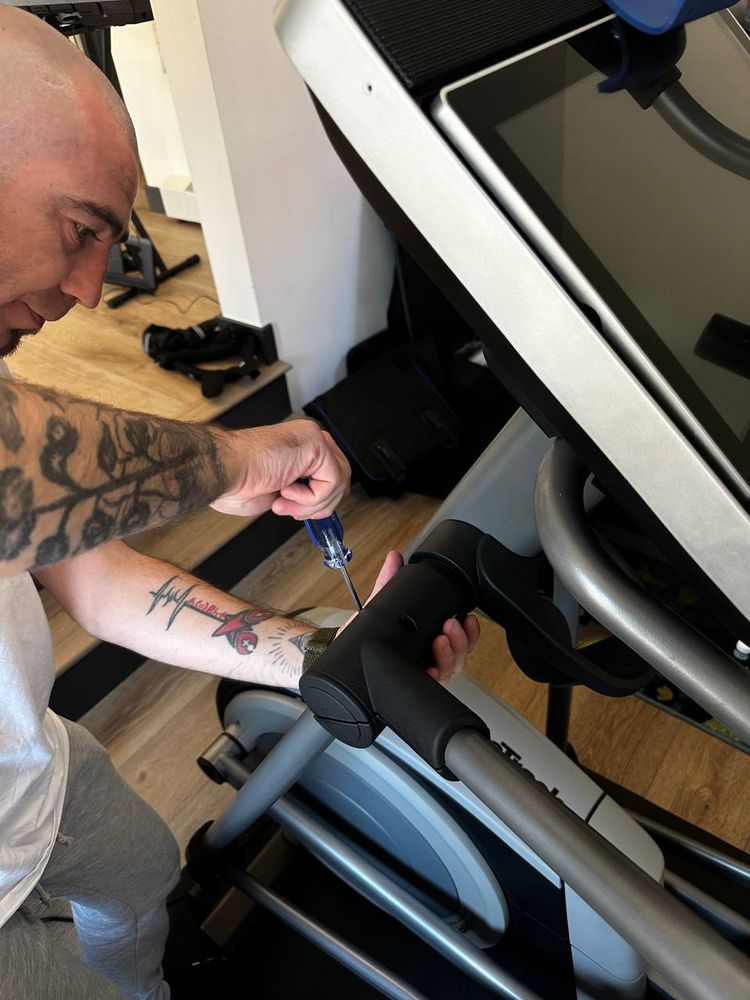 Technician tightening bolts on an exercise bike frame during assembly — equipment assembly service in Denver