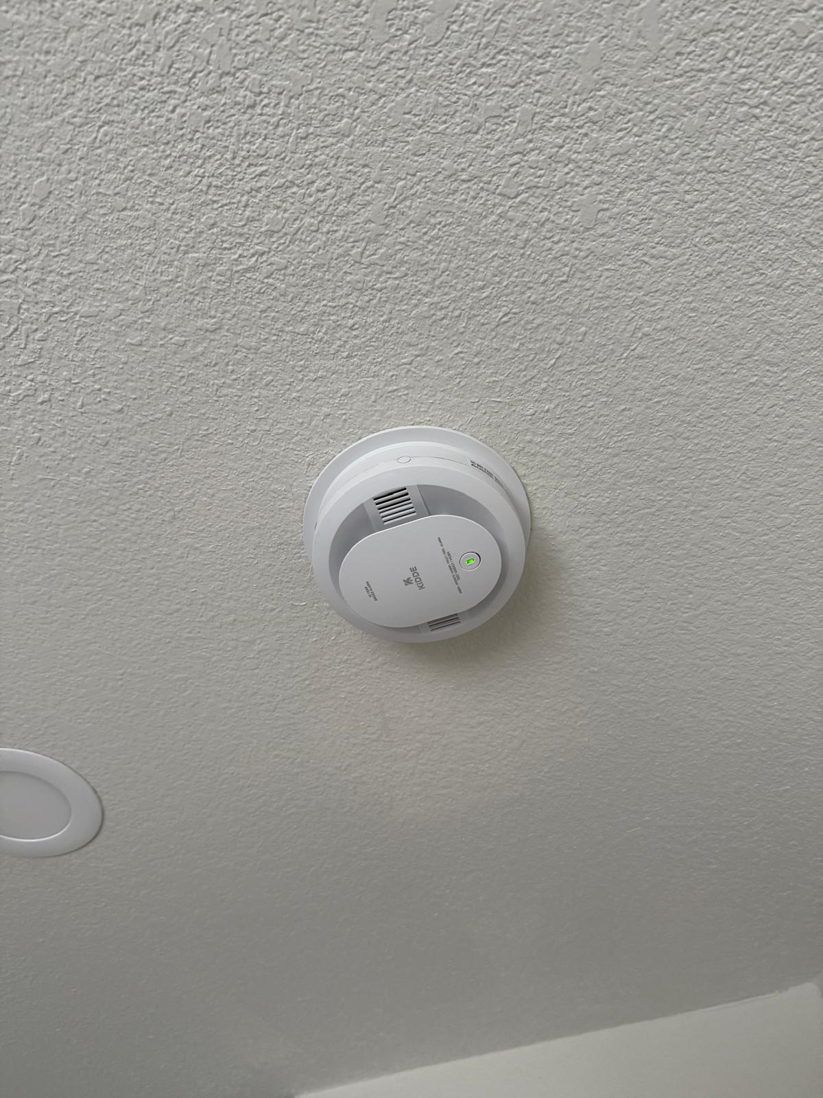 Round smoke detector fitted tight to a textured ceiling after replacement — fixture installation service in Denver