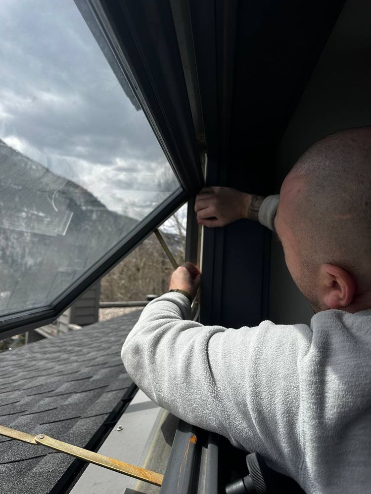 Technician reaching across a large sloped picture window to work the glass edge — window cleaning service in Denver