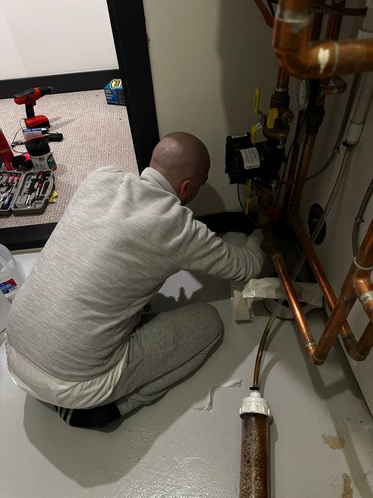 Technician working on valves and copper lines behind an access panel — plumbing repair service in Denver