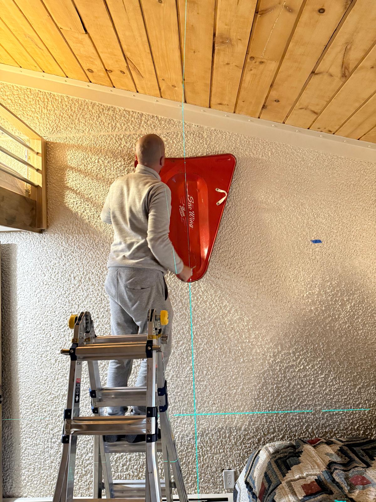 Technician on a step ladder mounting a large decorative panel to a wall — mounting and installation service in Denver