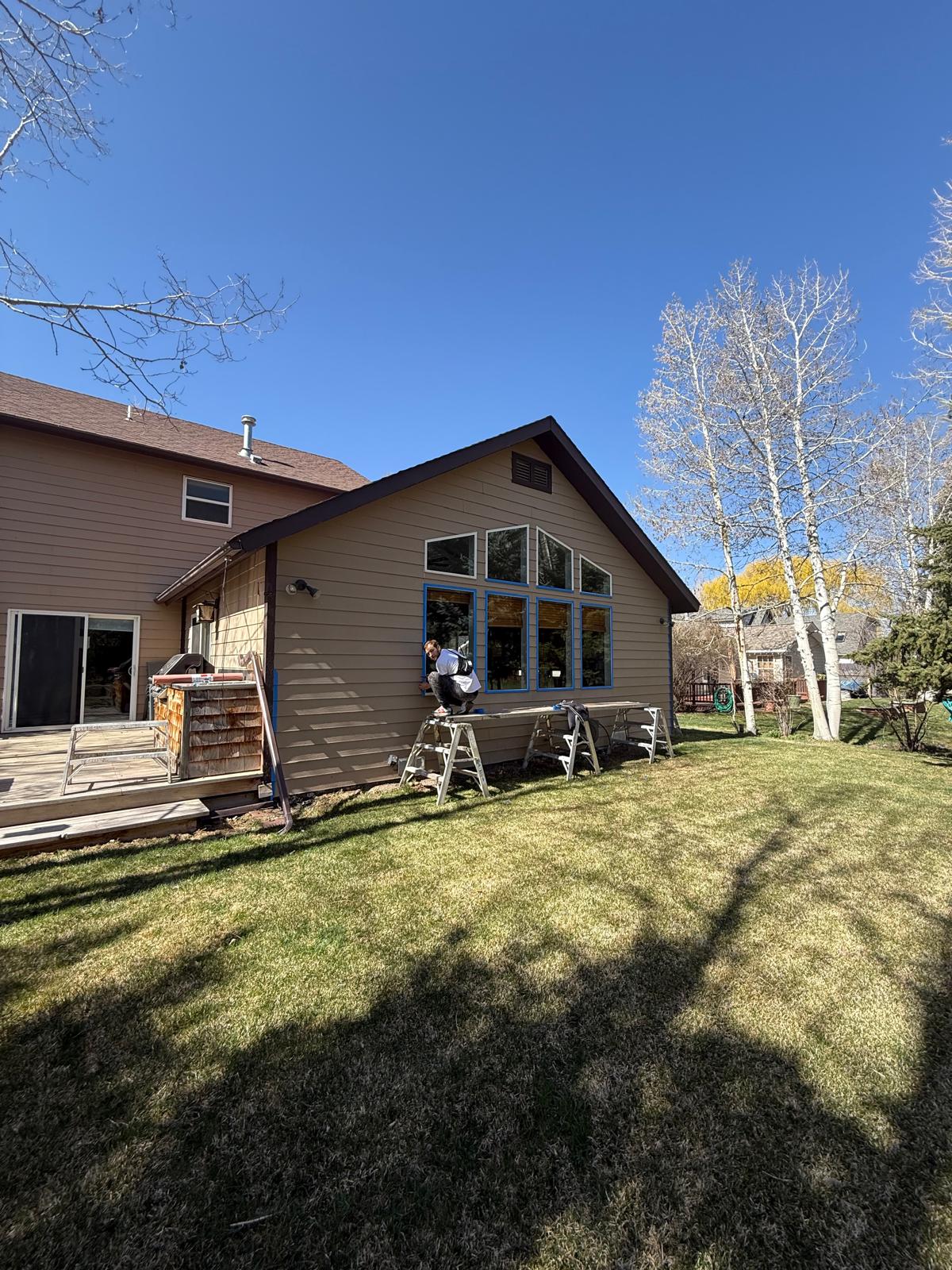 Two-storey home mid-repaint with ladders set against the gable end — exterior painting service in Denver